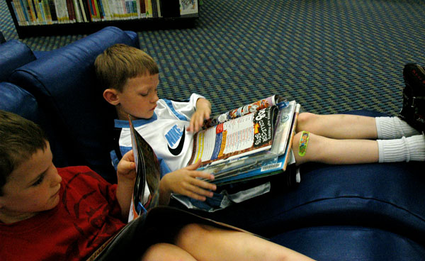 Two young boys sitting in reclining chairs reading books.