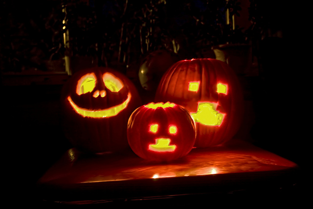 A group of three carved Halloween pumpkins glowing in the dark.