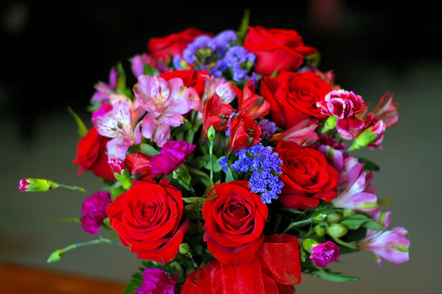 A flower bouqet filled with a mixture of red, pink and purple flowers.