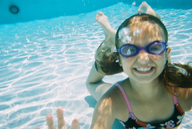Photo of a child underwater smiling and wearing swim goggles—representing one activity that promotes summer learning.