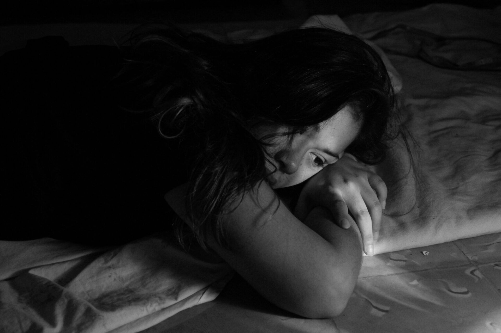 Black and white image of a woman resting on her stomach in her bed.