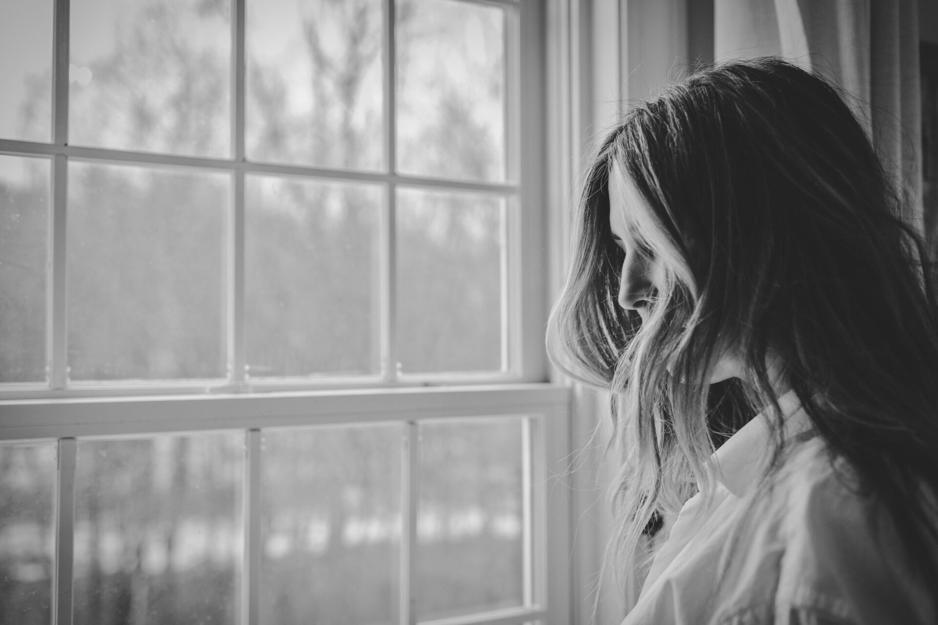 Black and white image of a woman looking out the window.