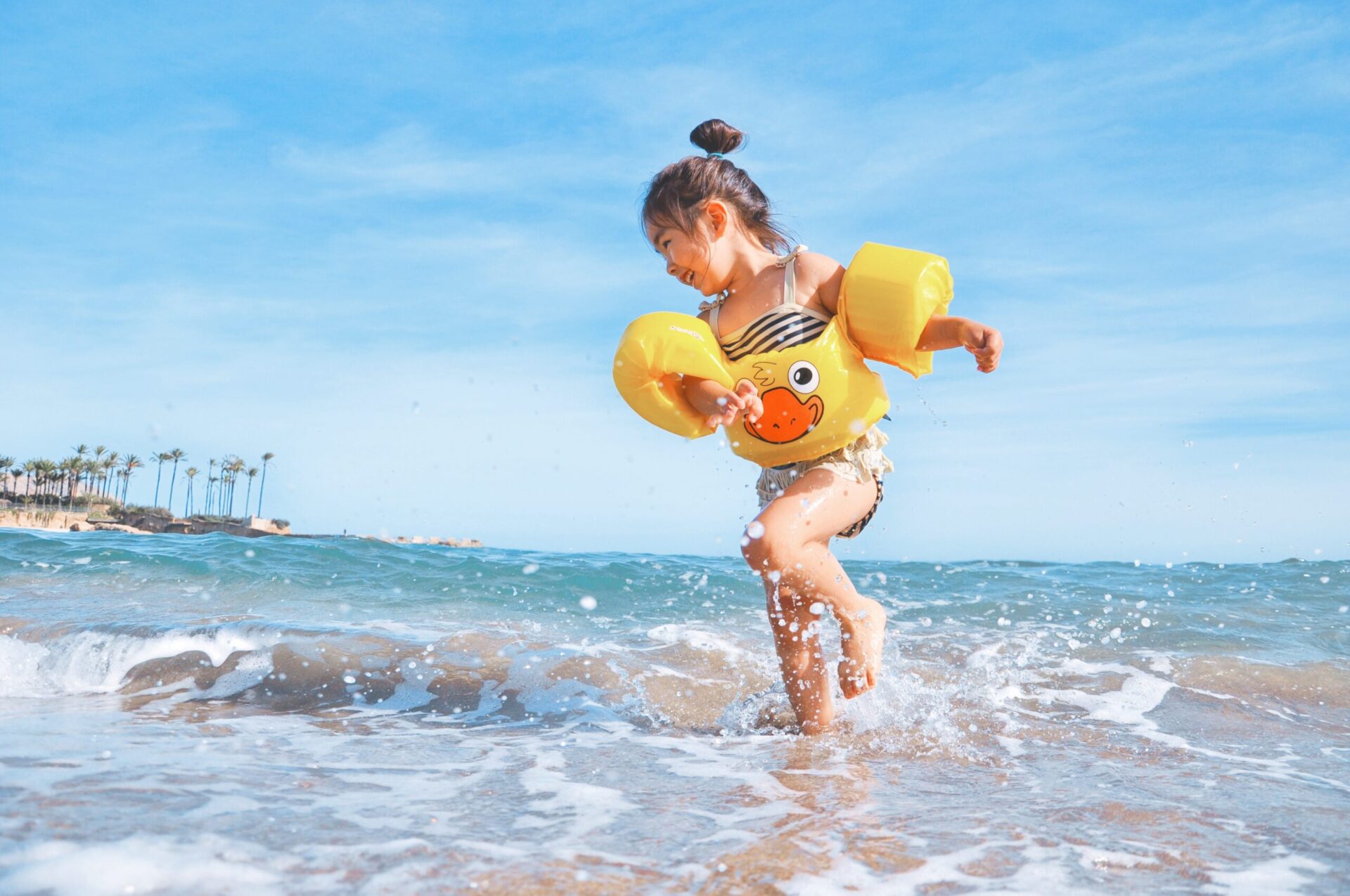 Young girl wearing yellow duck floaties plays in the small ocean waves.