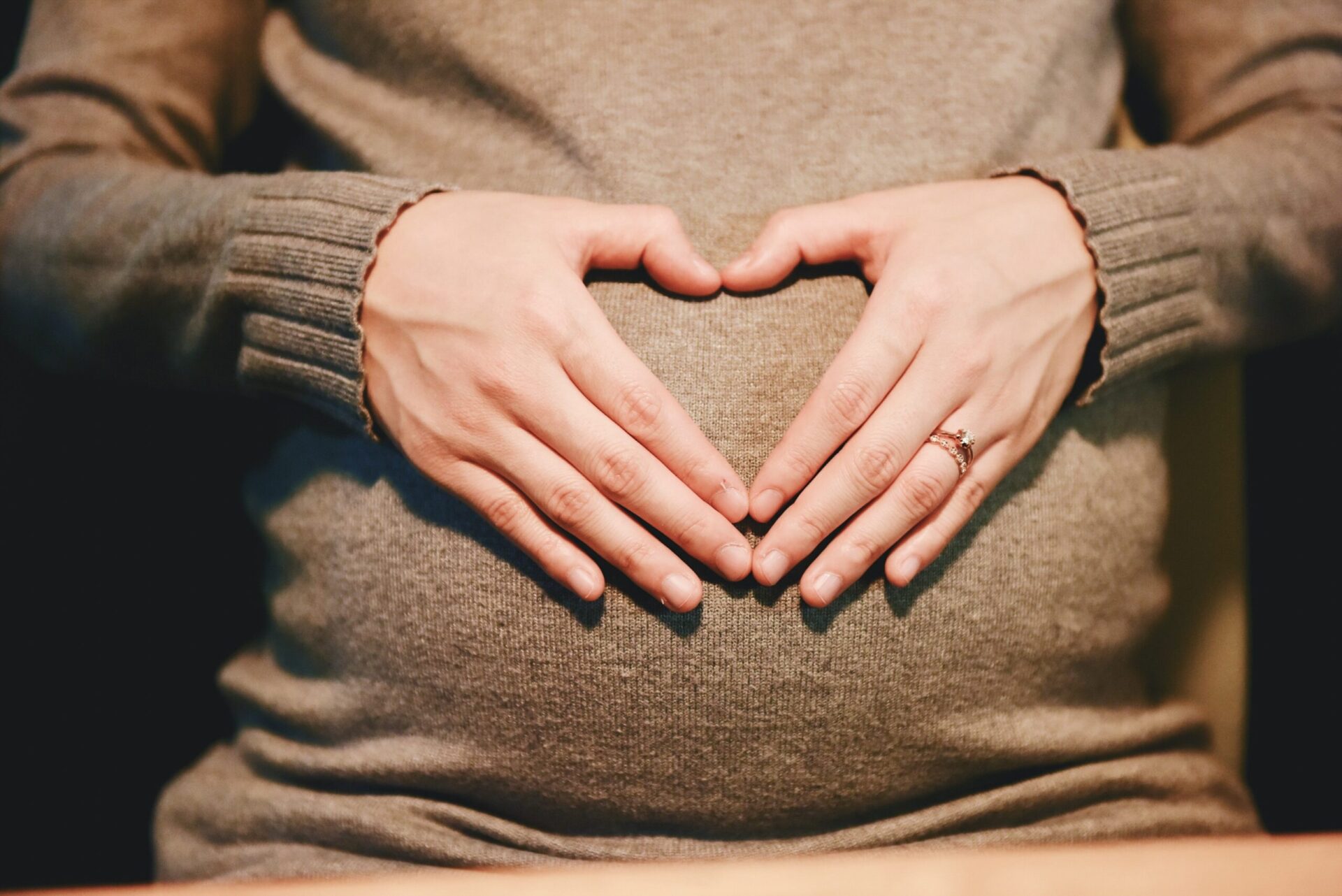 Close-up image of a woman holding her hands in the shape of a heart over her pregnant belly.