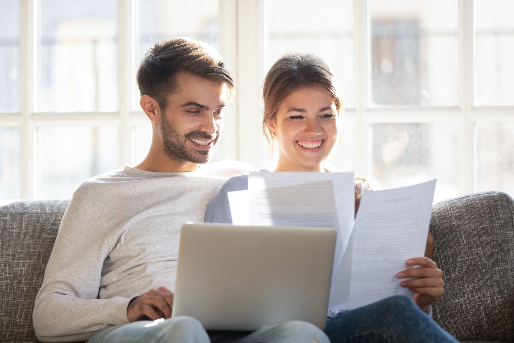 Smiling couple read paper documents on the couch together.