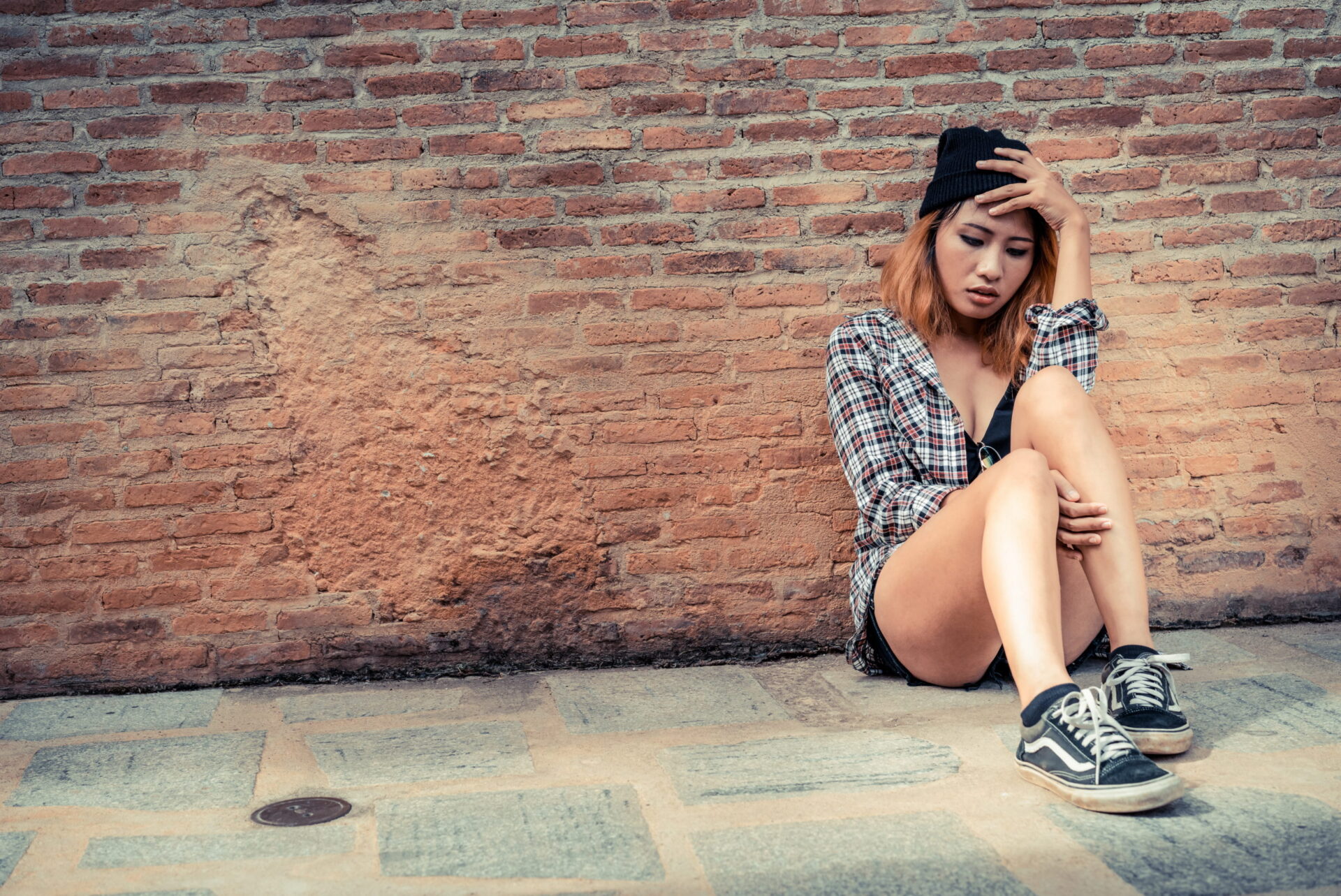 Depressed teenage woman feeling sad alone against brick wall in old town.