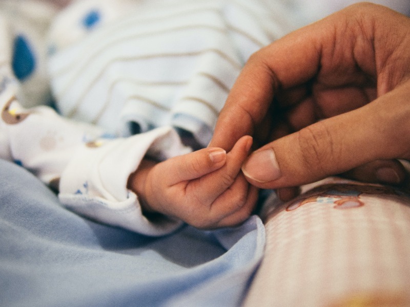 A parent holding the hand of their newborn baby.