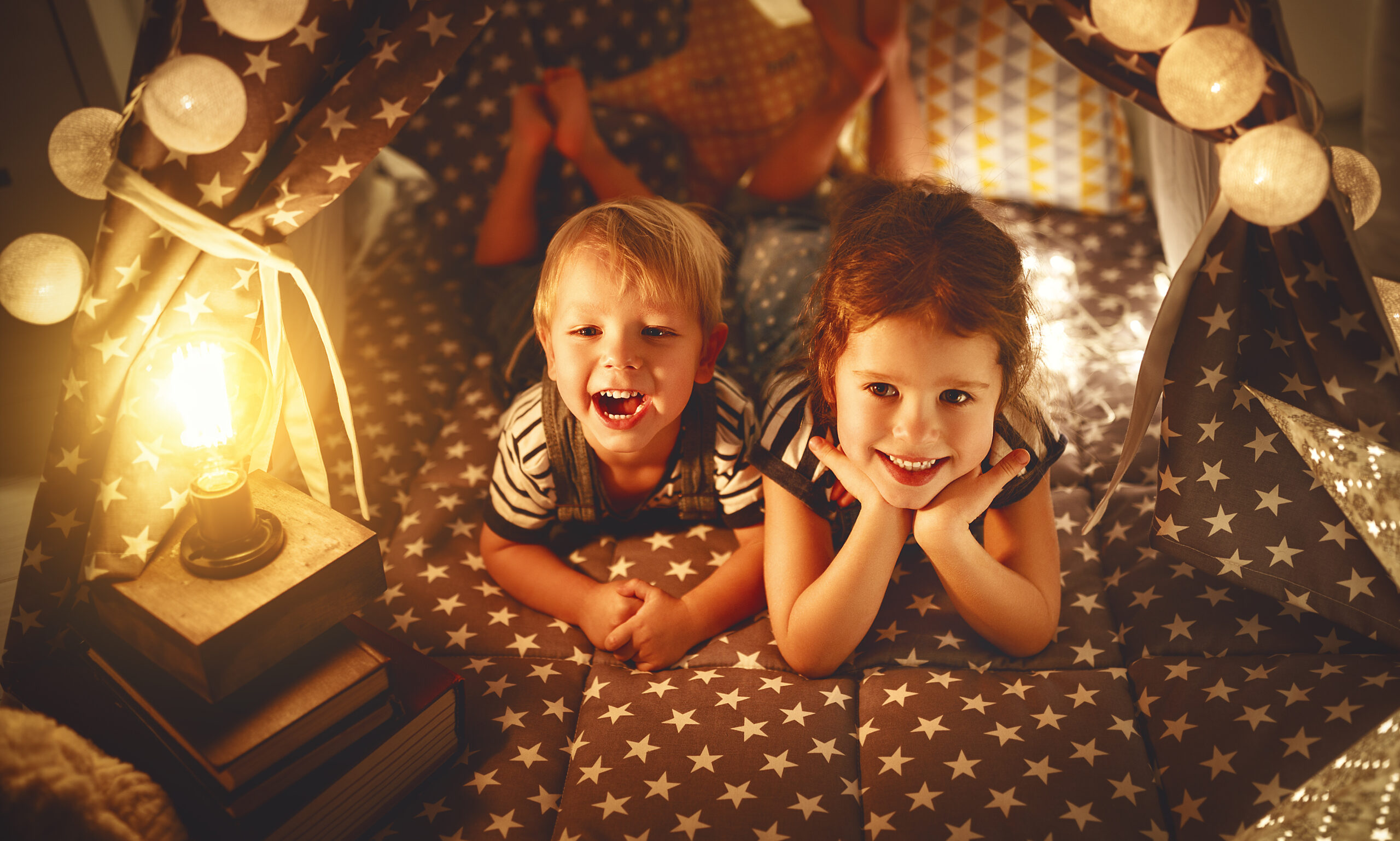 Two smiling children looking at the camera from a blanket fort