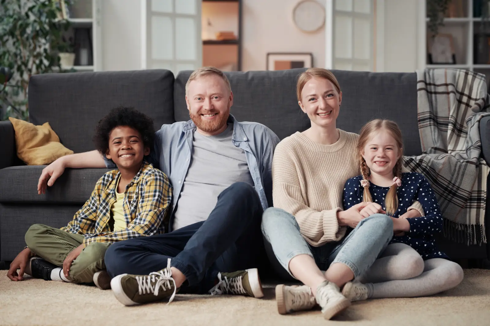 Post-Adoption Meetups With Kids. Portrait of happy family with adopted children sitting on floor in living room and smiling at camera