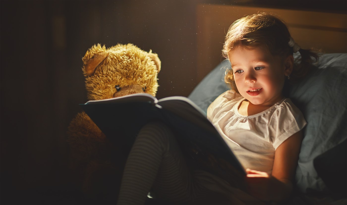 young girl from foster care reading a book to a teddy bear