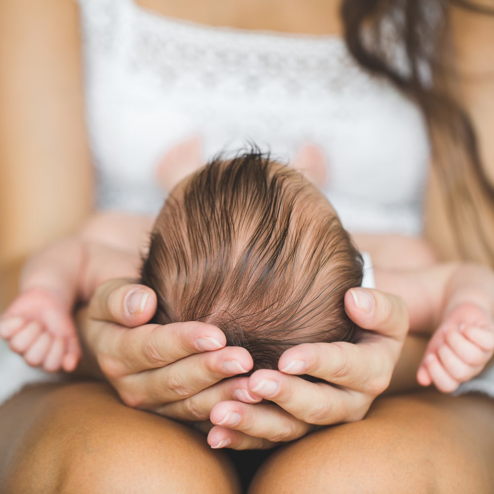 Color image in a circular frame of an infant's hand being held by an adult's hands